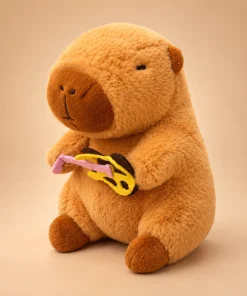 Capivara de pelúcia caramelo de 23cm vista de lado, segurando um acessório de feltro amarelo e rosa